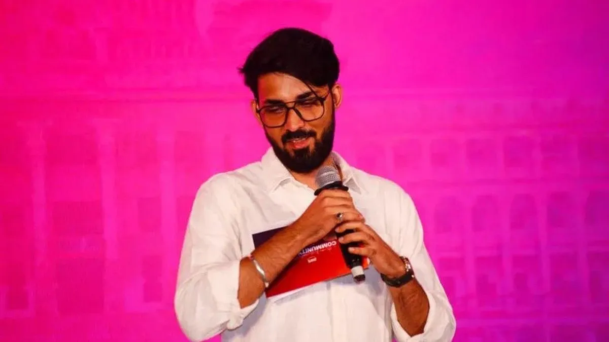 Ashutosh holding a microphone and a Community Day card on stage, in front of a pink backdrop.